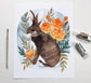 Watercolor painting of a rabbit with marigold flowers and leaves on a white background